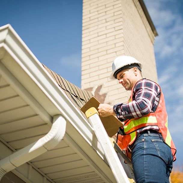 Man on a ladder checking the roof of a home